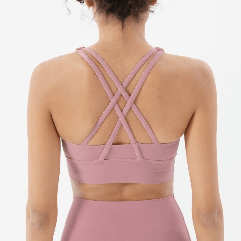 Woman wearing a pink nylon sports top with cross shoulder straps, providing comfort and support for fitness activities.